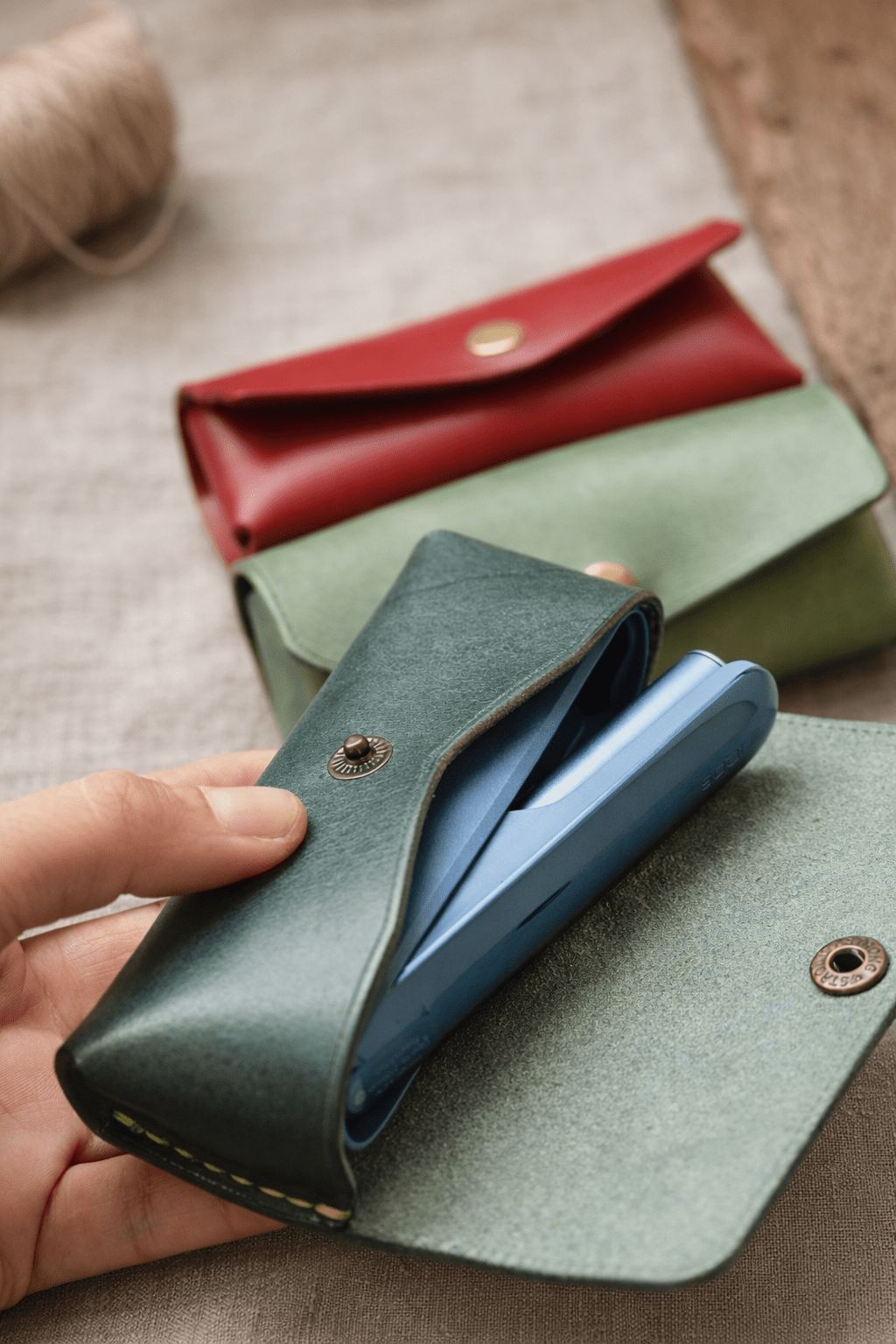 Кожен калъф за IQOS Iluma в ръка – устройството се вади от тъмнозелен калъф, ръчна изработка